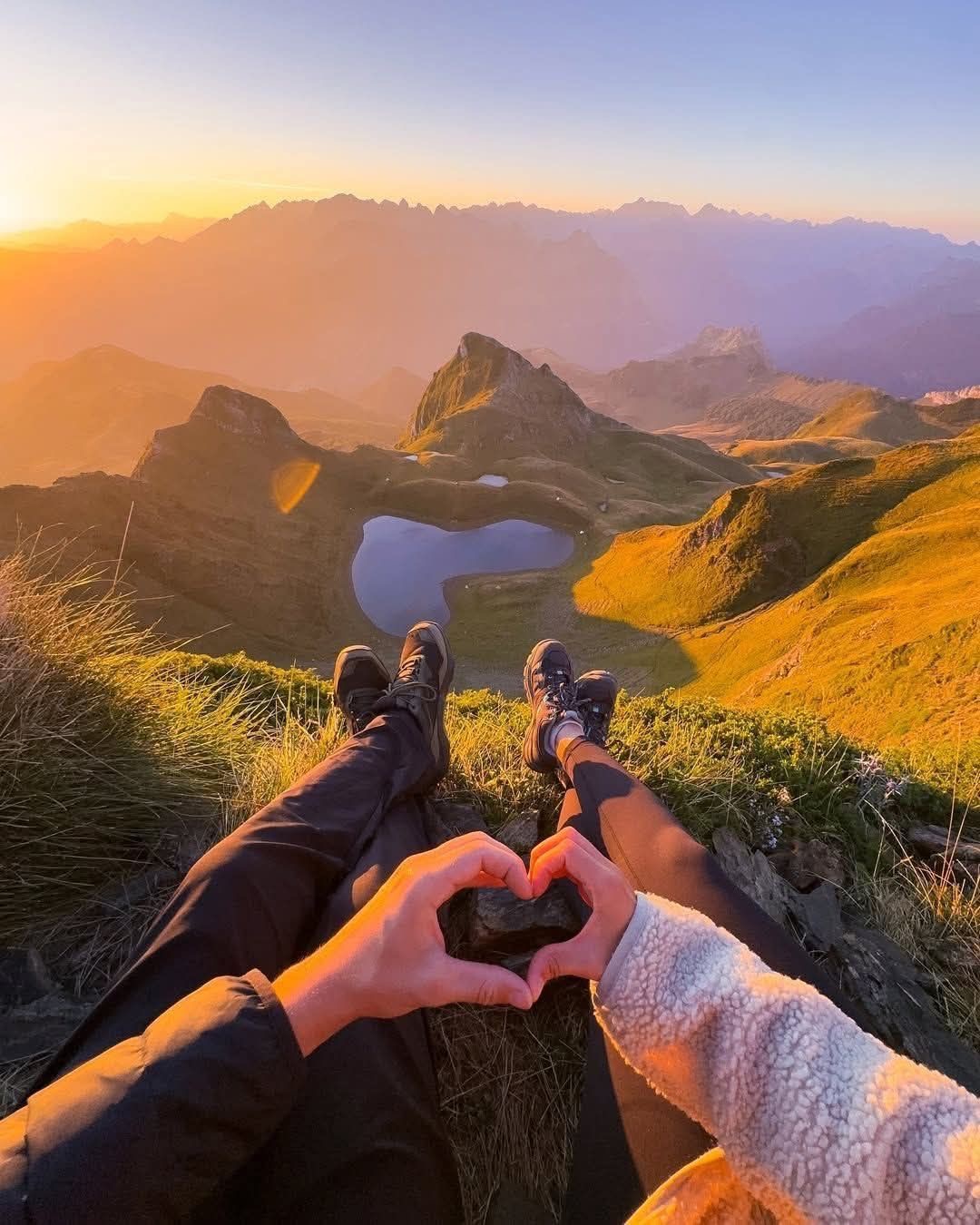 A couple sitting together above a mountain lake at sunrise
